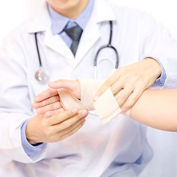 Male doctor putting gauze on young man's hand in clinic, closeup. First aid